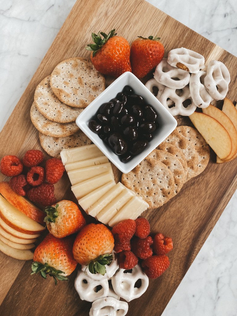 healthy valentines day snack board with fruit, cheese, and treats on a wood cutting board set on a white marble table