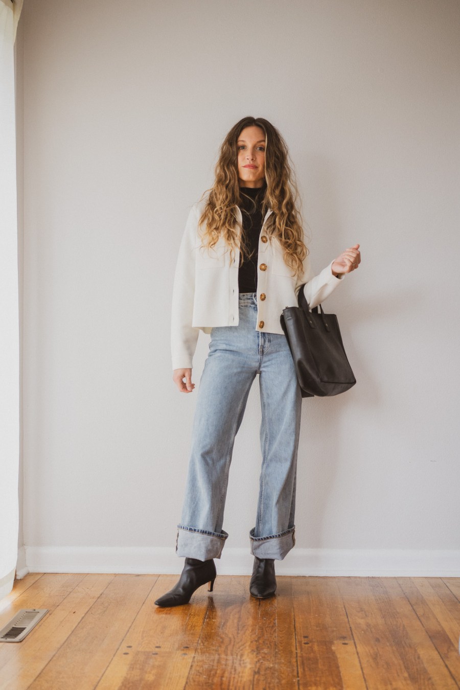 sézane betty cardigan outfit with a black turtleneck, light wash cuffed jeans, black boots, and a black tote bag